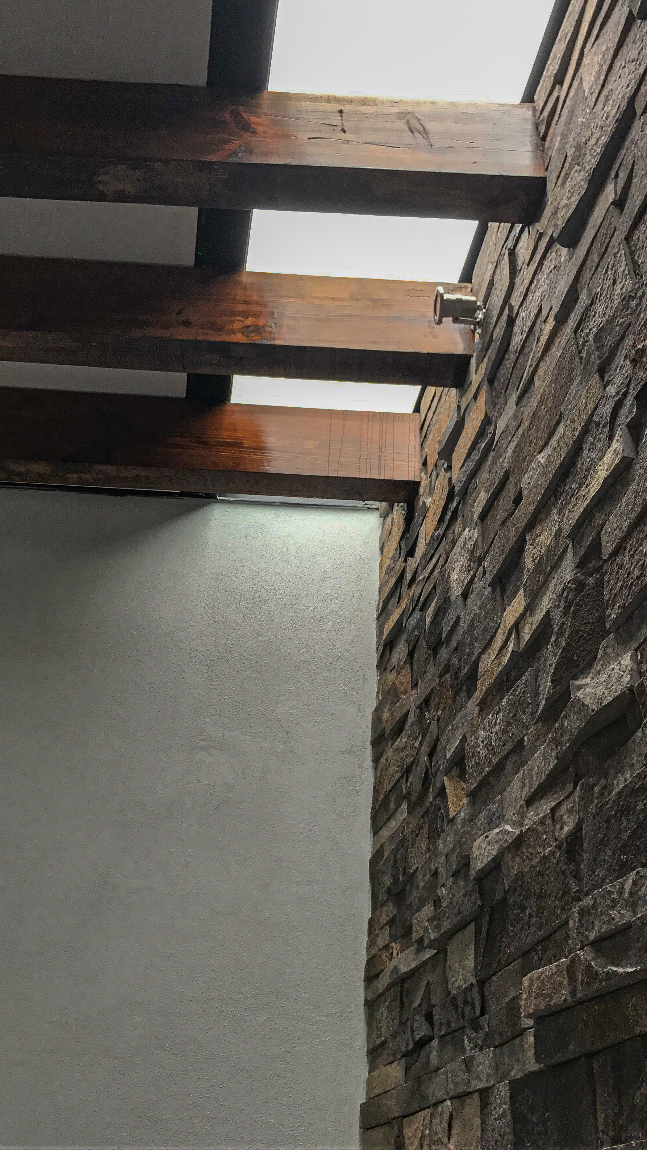 Detalle de muro de piedra natural en interior de Casa MG con iluminación empotrada, acabados residenciales Fer Et Ciment